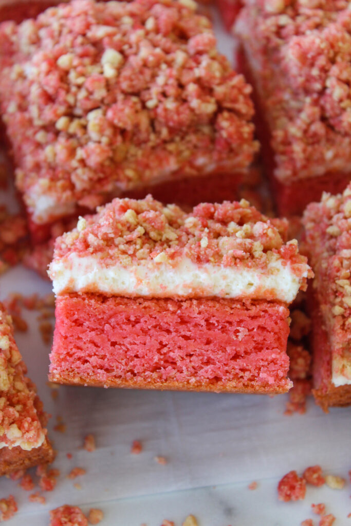 A brownie slice lifted showing layered strawberry brownie, cheesecake filling, and strawberry crunch topping