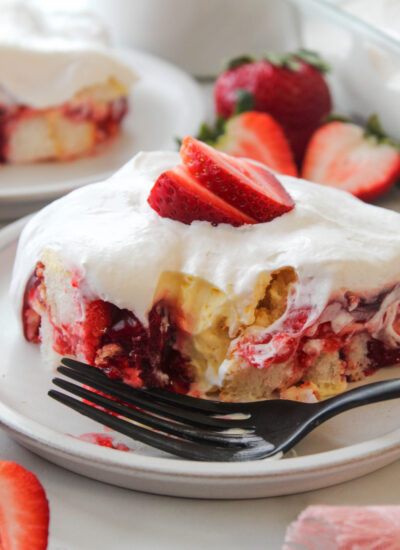 Sliced strawberry layer cake with white cream frosting and a strawberry on top, served on a plate with a black fork.
