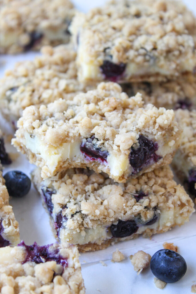 Layered blueberry cheesecake bars topped with a sweet crumble and whole blueberries

