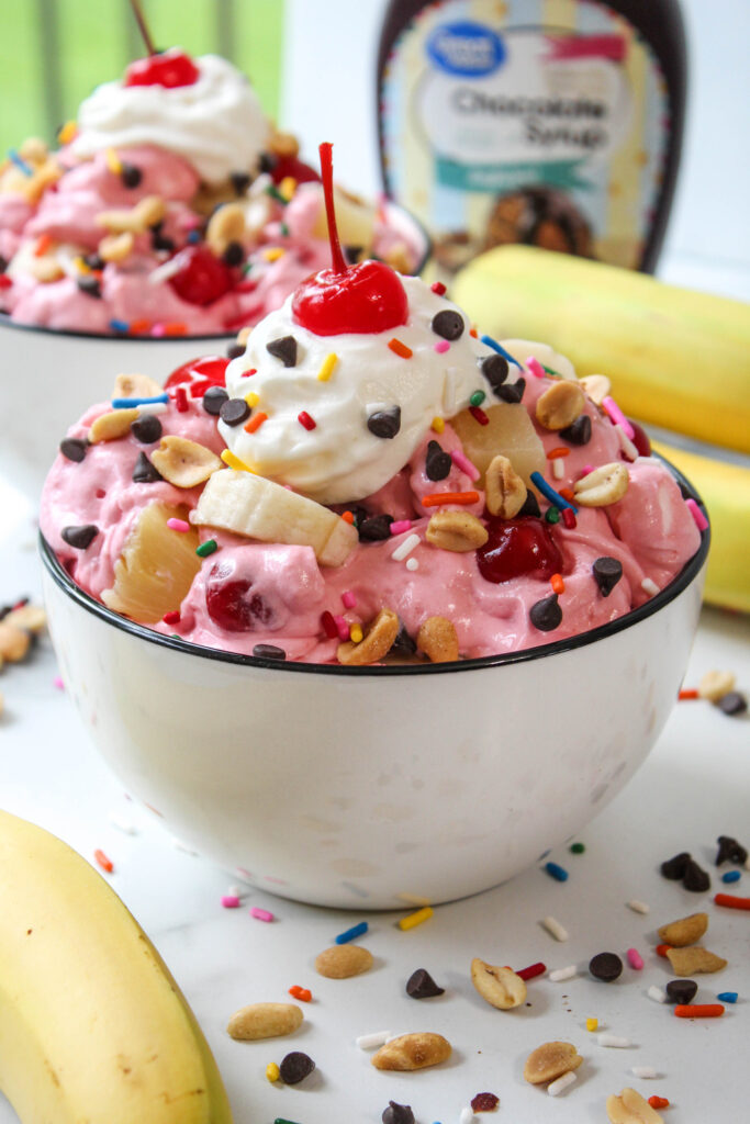 Colorful banana split fluff dessert with fresh bananas, pineapple, cherries, marshmallows, and whipped cream