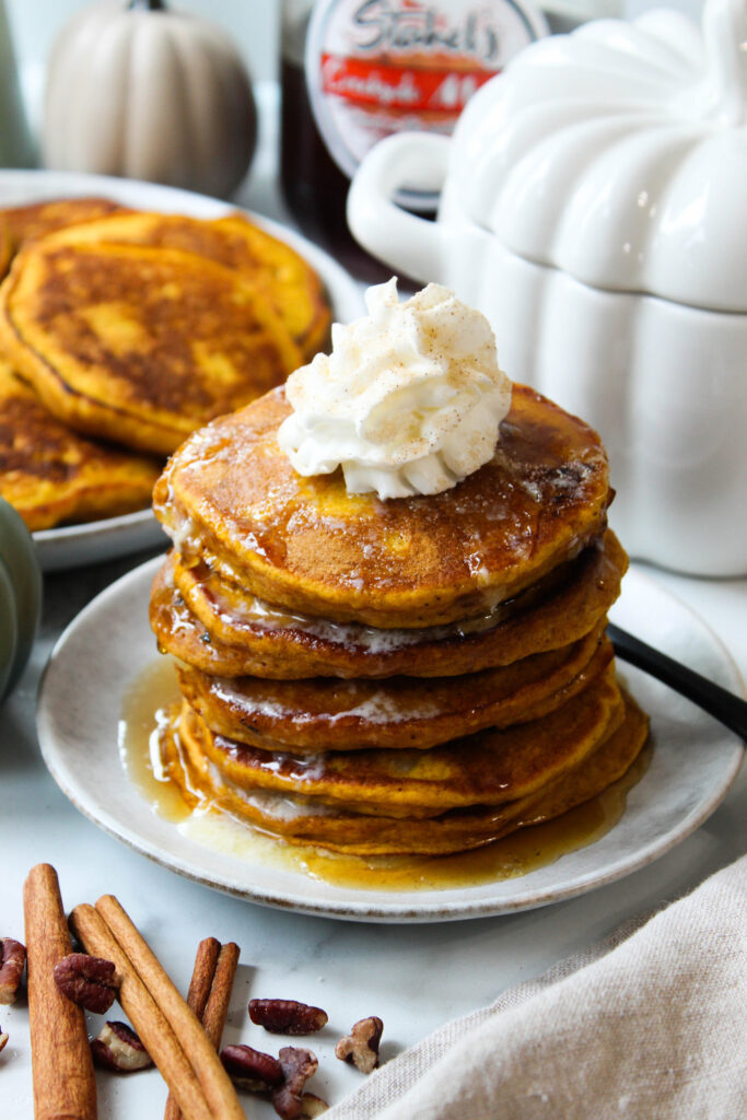 Fluffy pumpkin pancakes stacked high with maple syrup and butter