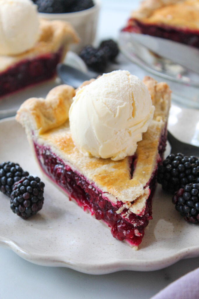 Slice of easy blackberry pie served on a white plate with fresh blackberries