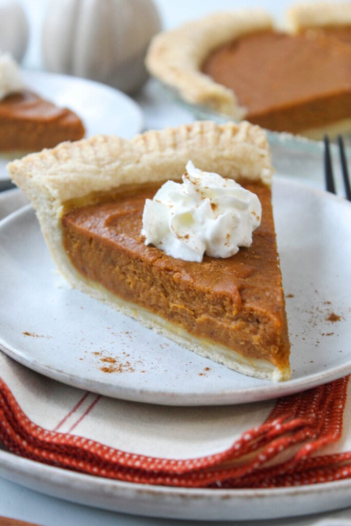 Slice of vegan pumpkin pie topped with dairy-free whipped cream