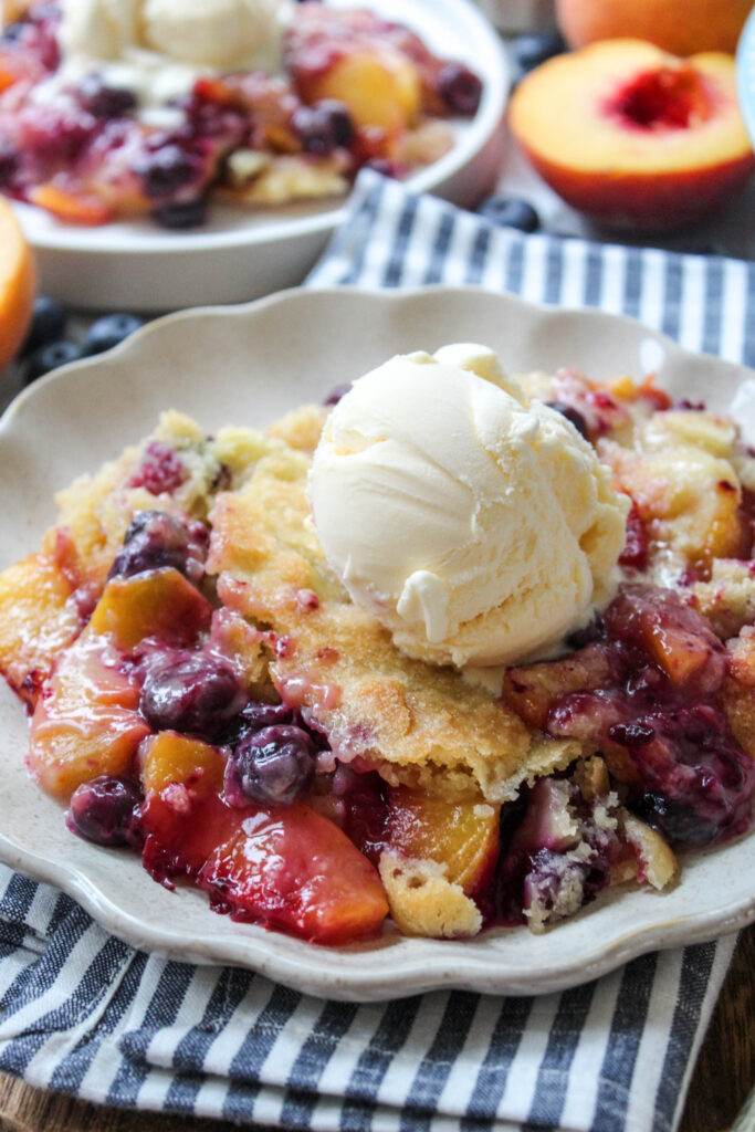 Spoonful of warm peach blueberry cobbler revealing the syrupy fruit underneath