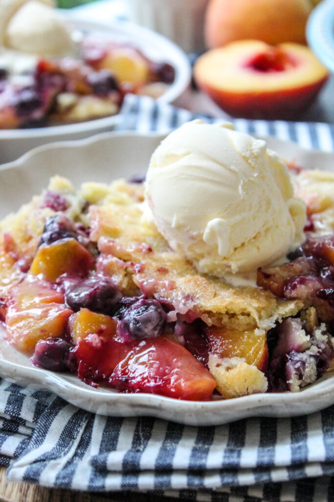 Peach blueberry cobbler served in a bowl with a scoop of melting vanilla ice cream