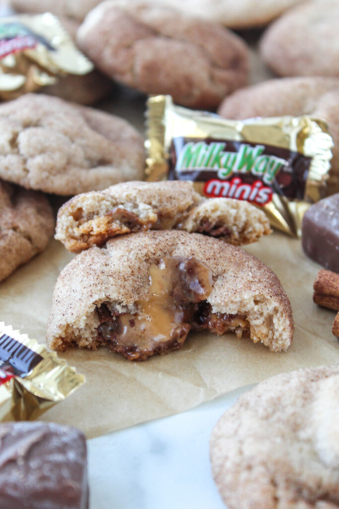 Milky Way stuffed snickerdoodle cookies dusted with cinnamon sugar, broken open to reveal a gooey caramel and chocolate center
