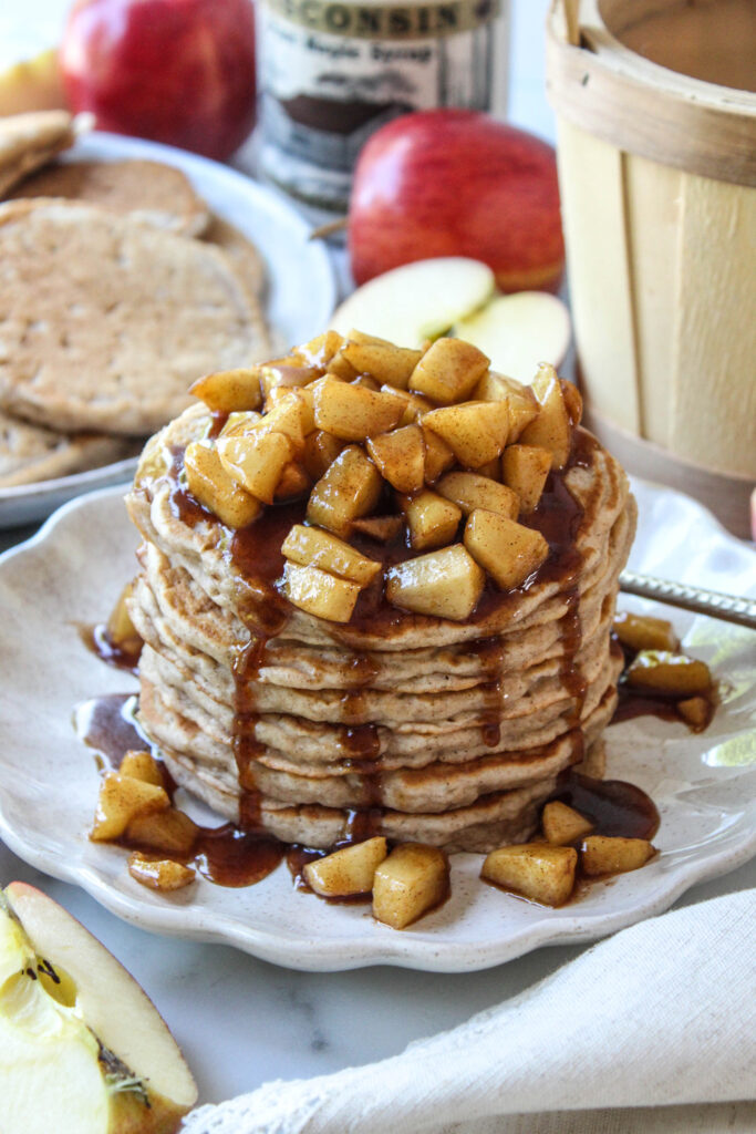Stack of fluffy apple cinnamon pancakes topped with maple syrup and fresh apple slices