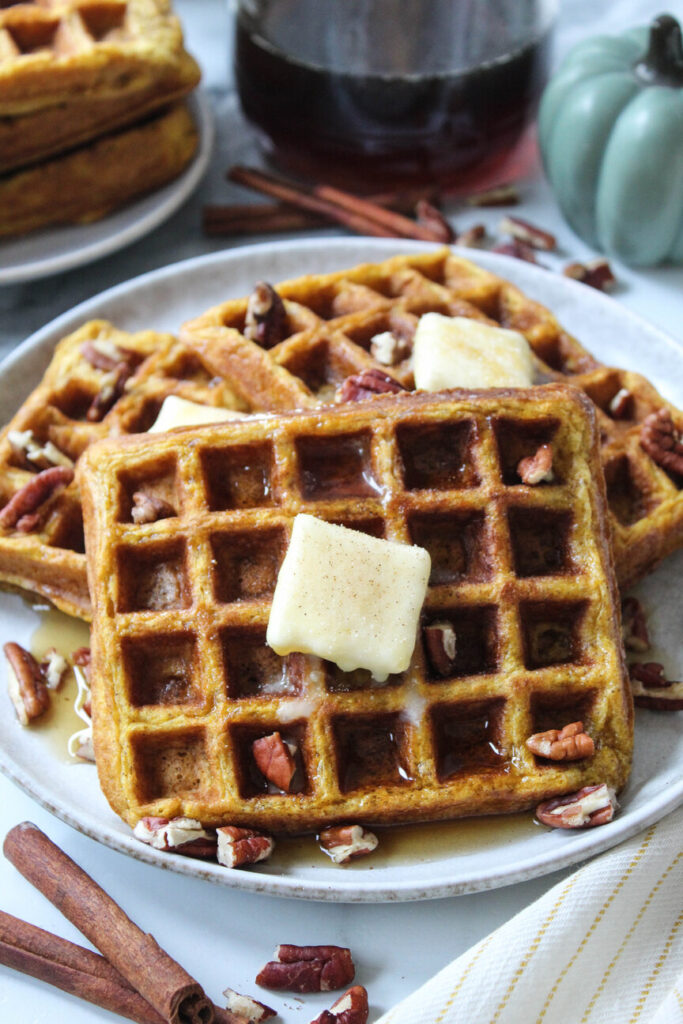 Golden pumpkin waffles stacked on a plate with maple syrup