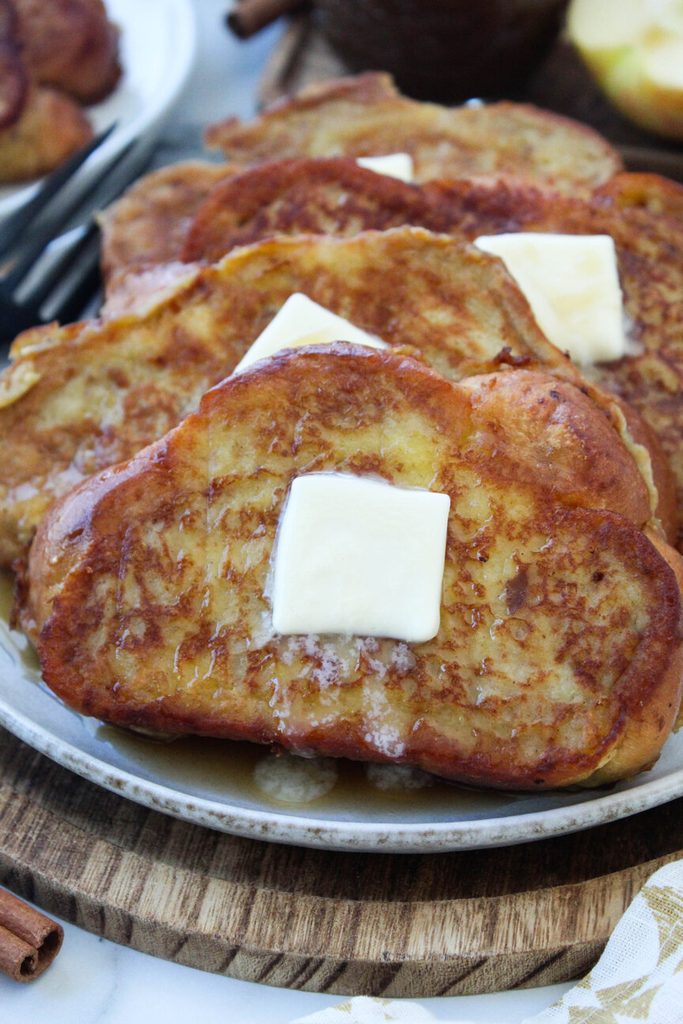 Apple butter French toast stacked on a plate with a drizzle of warm maple syrup