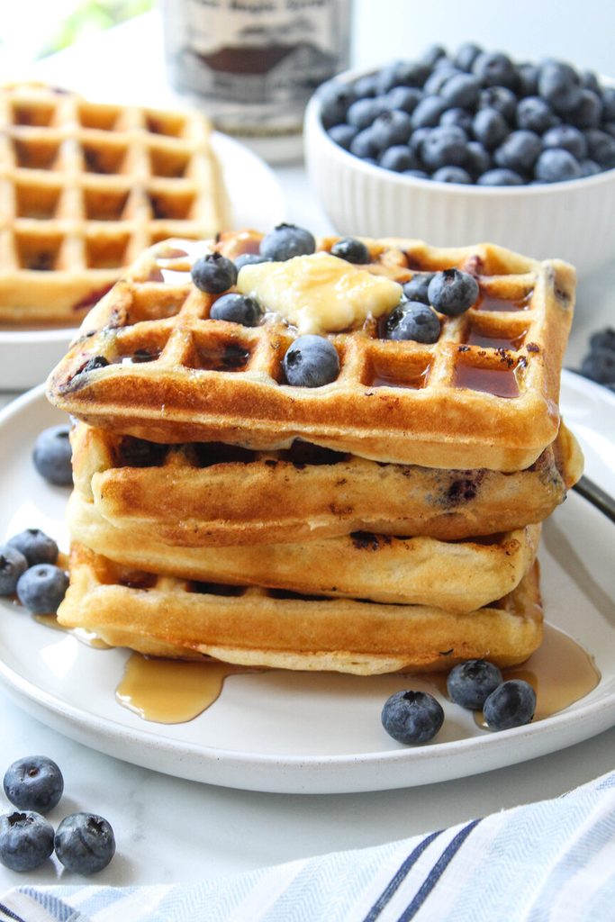 Stack of blueberry waffles topped with fresh berries and maple syrup