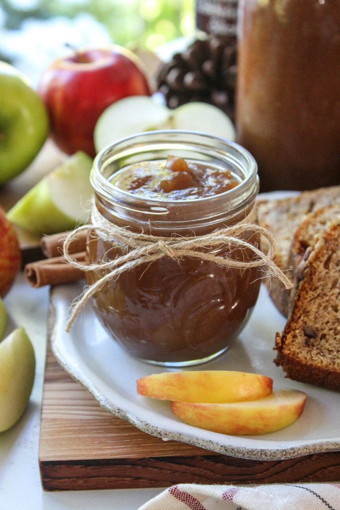 Dark, glossy apple butter in a mason jar beside fresh apples